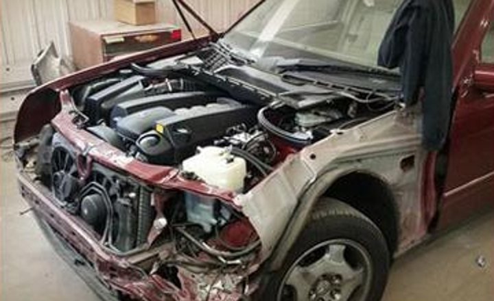 A badly damaged red sedan before repair
